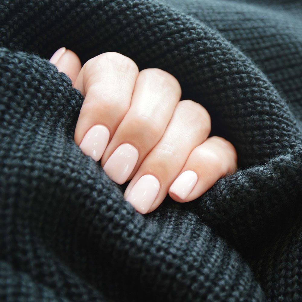 Female hands with a neat beige manicure in a black knitted sweater. Winter hand care, gel polish, shellac.